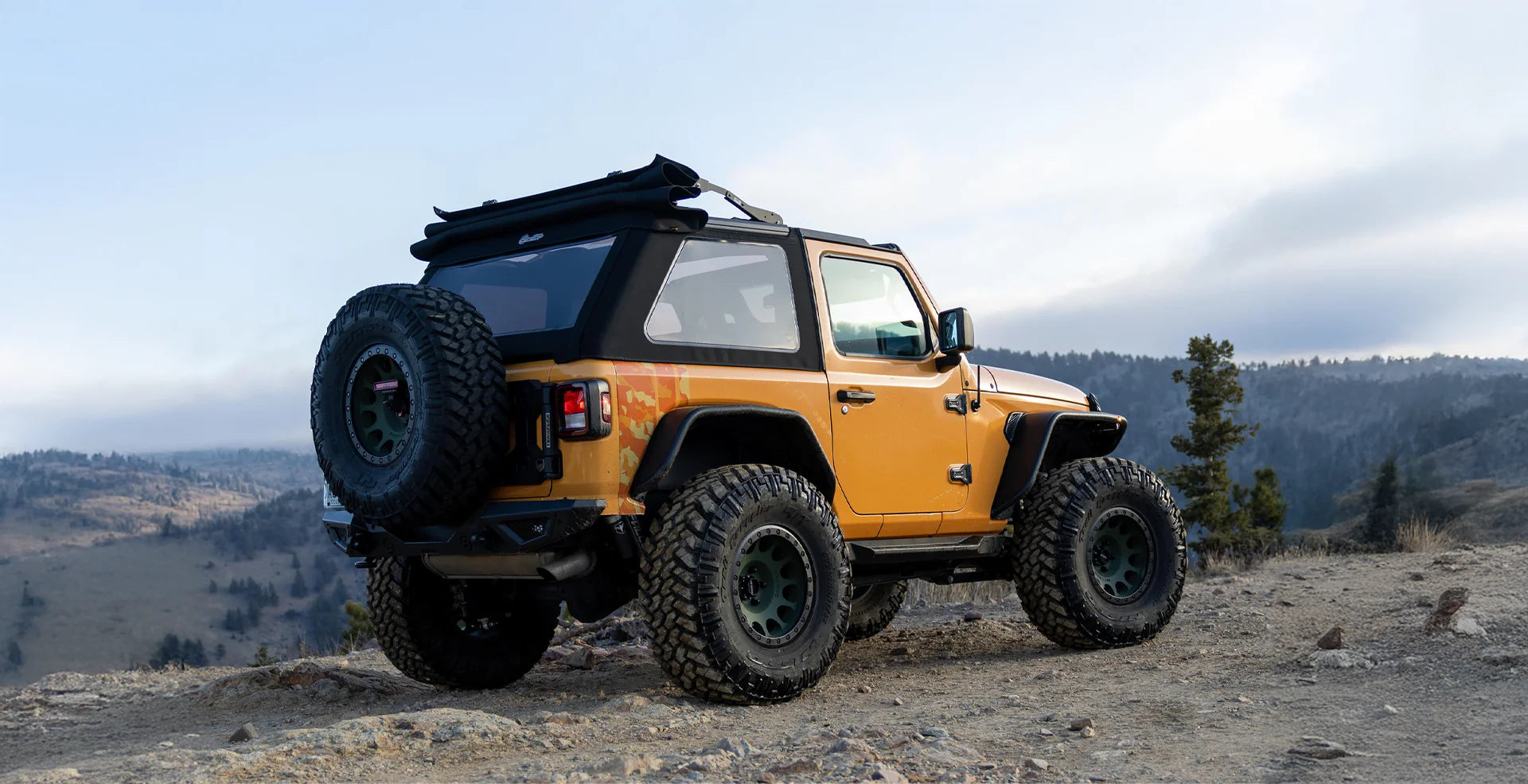 Jeep Wrangler JL 2‑Door fitted with premium soft top, mesh sun panel and adventure‑ready hardware parked on off‑road trail