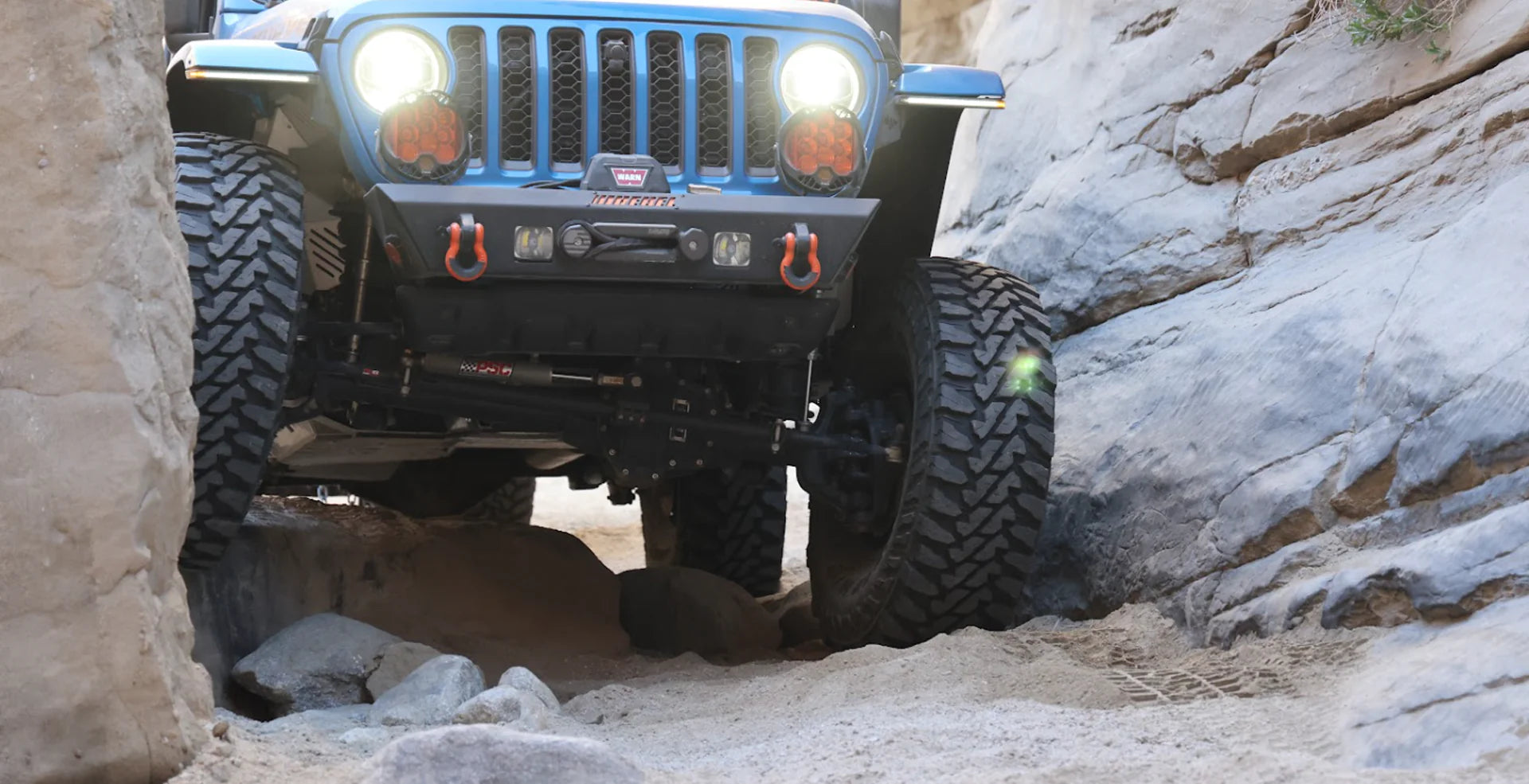 Jeep Wrangler JL fitted with adjustable front and rear track bars on lifted suspension driving on rugged off‑road terrain